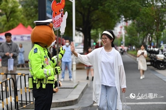 6月7日上午9時(shí)，隨著鈴聲的響起，2023年江西高考正式開(kāi)考，江西省的53.57萬(wàn)考生以縣（區(qū)）為單位隨機(jī)安排在全省256個(gè)考點(diǎn)、18968個(gè)考場(chǎng)參加高考。圖為“小熊交警”和考生擊掌鼓勵(lì)。 人民網(wǎng)記者 時(shí)雨攝