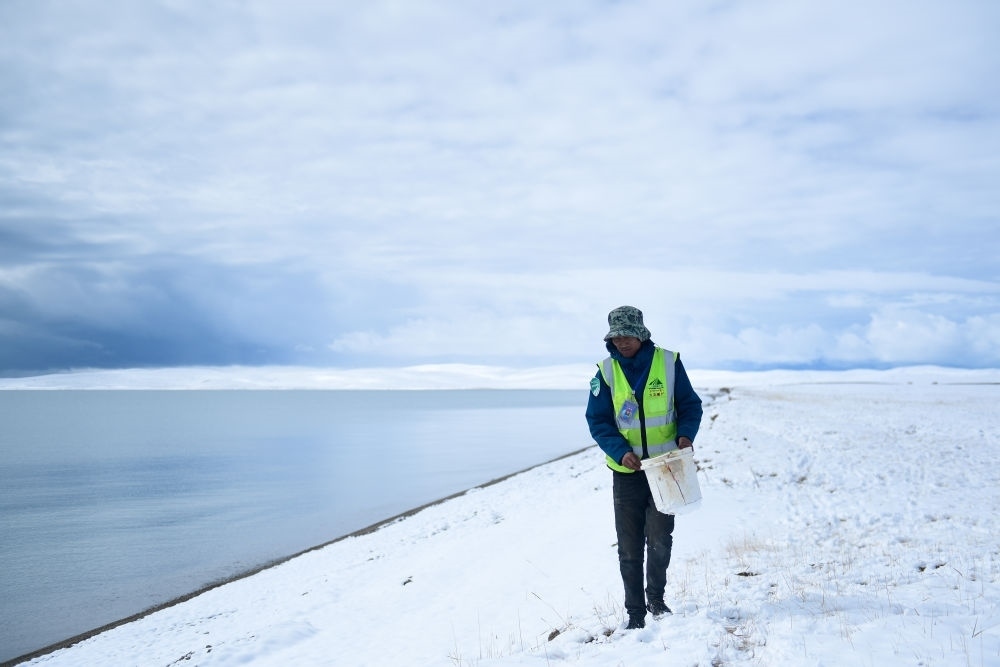 2021年10月20日，在青海省果洛藏族自治州瑪多縣扎陵湖鄉(xiāng)勒那村，三江源國家公園黃河源園區(qū)生態(tài)管護(hù)員在扎陵湖邊撿拾垃圾。新華社記者 張龍 攝
