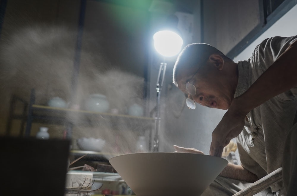 ↑ 在景德鎮(zhèn)，手工匠人吹去坯內(nèi)的泥土（2021年7月14日攝）。