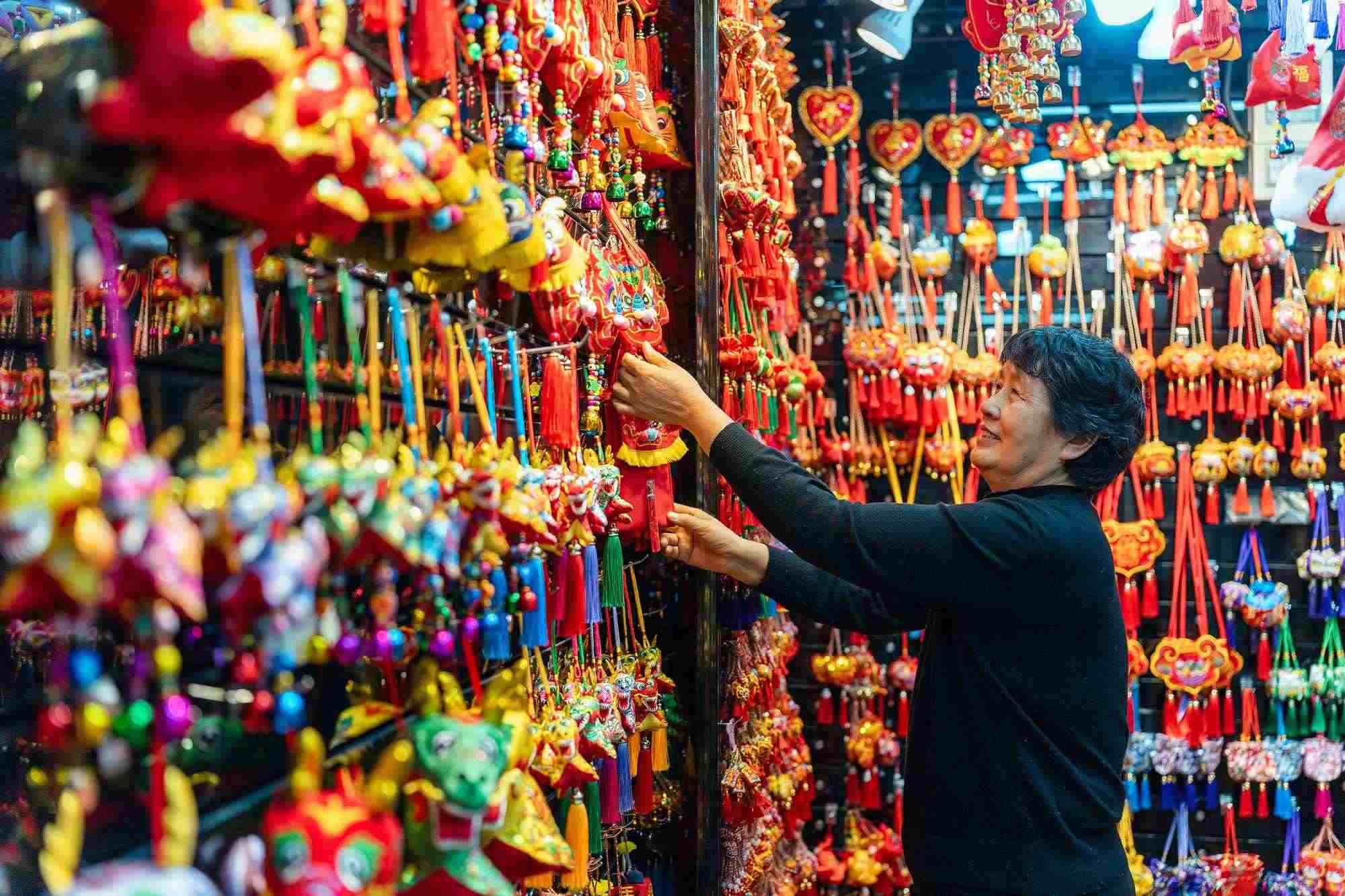 2023年12月11日，金華義烏國際商貿(mào)城，龍年喜慶用品掛滿攤位，顧客正在挑選中。