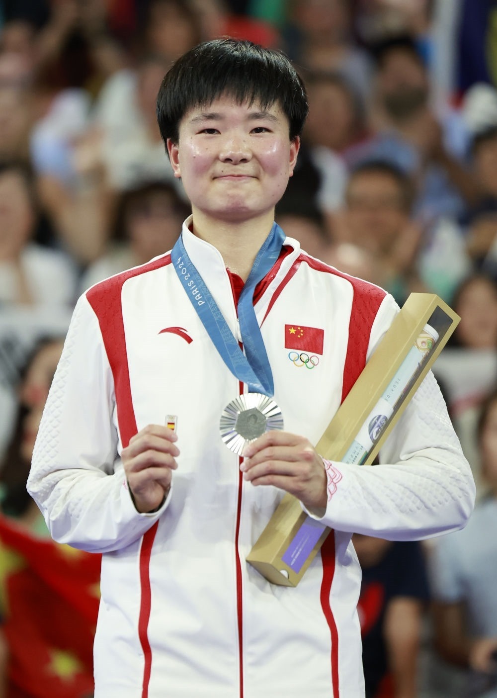 巴黎奧運(yùn)會羽毛球女子單打亞軍、中國選手何冰嬌在頒獎儀式上一手握著銀牌，一手握著西班牙奧委會徽章（2024年8月5日攝）。新華社記者 任正來 攝