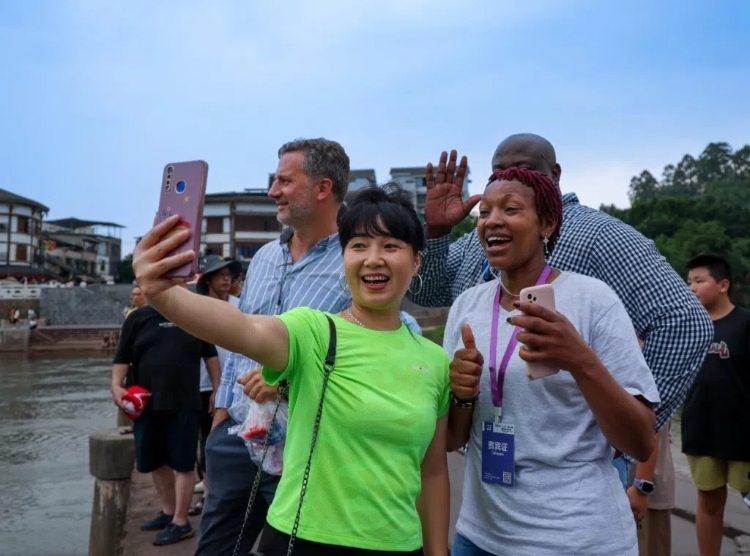 2024“一帶一路”媒體合作論壇聯(lián)合采訪調(diào)研行成員在樂山蘇稽古鎮(zhèn)與游客合影留念。本報記者 伊霄攝