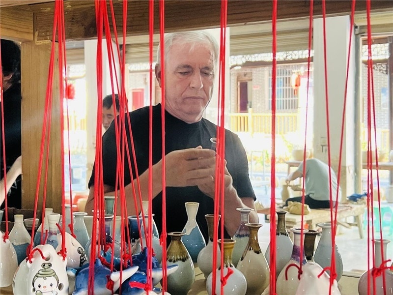 鄉(xiāng)愁如同一根根紅線，將游子與故鄉(xiāng)永遠(yuǎn)地牽連到一起?；逄账囄幕瘎?chuàng)意一條街的母氏陶藝館內(nèi)，紅線吊著陶瓶，思緒游走萬里。摩爾多瓦“信息標(biāo)簽”通訊社社長(zhǎng)亞歷山大·塔納斯端詳著館內(nèi)展示的陶藝作品，并挑選出心儀的小擺件帶回摩爾多瓦，也帶走花茂村的“鄉(xiāng)愁”。（張亞欣攝）