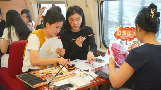 10月1日，旅客們?cè)贕1634次列車上給油紙傘作畫(huà)。新華社記者周義 攝